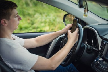 Genç şoför direksiyonun başında tek eliyle akıllı telefonunu kullanırken telefonu yüzünden dikkati dağılmış. Yolda risk ve tehlike durumları, trafik kurallarının ihlali