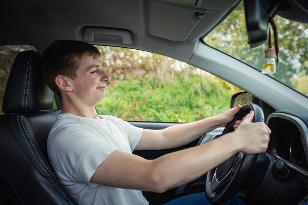 Proud and cheerful young driver in front of the steering wheel driving his new car confidently