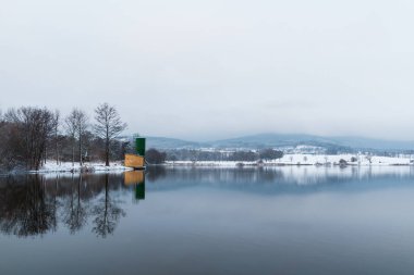 Fishing granary building on pond shore in winter czech landscape. Calm reflection scene
