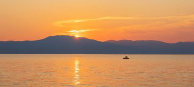 Gün batımı gökyüzü ve uzak tepe ile küçük tekne silueti denizde yüzüyor. Seyahat, spor geçmişi, Hırvatistan, ada Krk