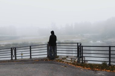 Genç adam tırabzanın önünde duruyor ve şehirde Vltava Nehri 'ni arıyor Ceske Budejovice sisle