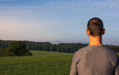 Güneşin doğuşunda sisli bir sabah manzarasında yürüyen adam seçici bir şekilde manzaraya odaklanıyor.