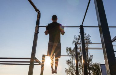 Fitness adamı gün doğumunda oyun parkında barfiks çekiyor. Sabah rutini, zihinsel ve fiziksel güç, sağlıklı yaşam tarzı