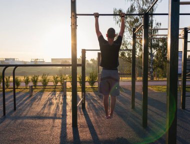 Fitness adamı gün doğumunda oyun parkında barfiks çekiyor. Sabah rutini, zihinsel ve fiziksel güç, sağlıklı yaşam tarzı