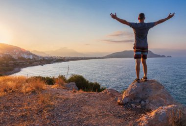 Elleri havada kayaların üzerinde duran adam, Türkiye 'nin Alanya kentini izlemenin tadını çıkarıyor