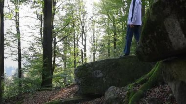 Sonbahar ormanında kapüşonlu ve pantolonlu bir adam taşın üzerinde yürüyor. Yavaş çekim, Çek manzara geçmişi