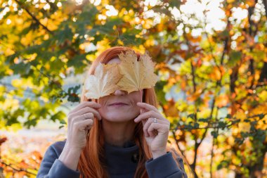 Genç kızıl saçlı güzel bir kadın sonbahar yaprağını tutuyor. Yaşam tarzı, meçhul arkaplan