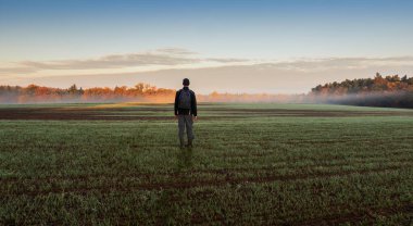 Wellington botlu bir adam sonbahar sahasında renkli ağaçlar ve sis ile dikiliyor. Çek manzarası