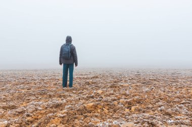 Sırt çantalı bir adam sisli buzlu alanda yürüyor.