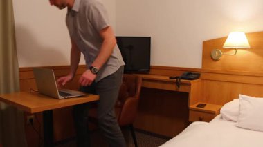 Bir adam otel odasında bir sandalyeye oturur ve çalışır, dizüstü bilgisayarında rahatlar, interneti araştırır.