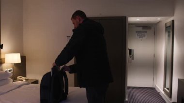 Sırt çantasına defter koyup otel odasından ayrılan bir adam. Seyahat, konaklama geçmişi
