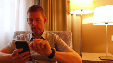 Bir adam otel odasında bir sandalyeye oturur ve çalışır, dizüstü bilgisayarında rahatlar, interneti araştırır.