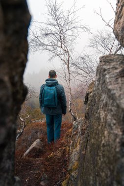 Ceketli ve sırt çantalı genç adam sisli bir sabahta kaya arazisinde yürüyor. Keşfet, tek başına yolculuk geçmişi