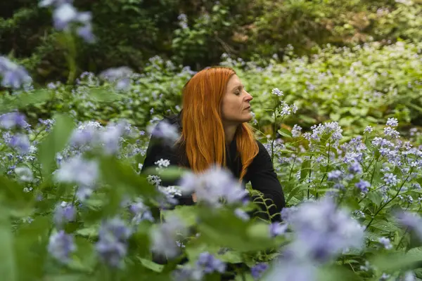 Kızıl saçlı kadın portresi. Gözleri kapalı. Ormandaki uzun ömürlü çiçek tarlasında oturuyor.