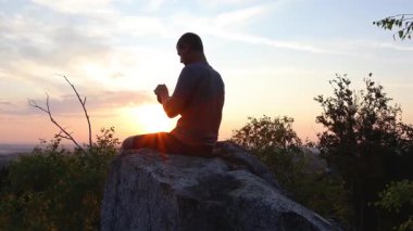 Adam gün batımında kayarken, cep telefonunda dolaşırken kaya taşının üzerinde rahatlıyor. Teknoloji, cep telefonunu doğada kullanmak, yan kamera hareketi