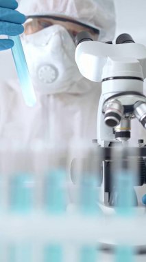 Bilimadamı laboratuvarda numune inceliyor. Uzman bilim adamı mikroskop yakınında bir test tüpü örneğini dikkatlice analiz ediyor..