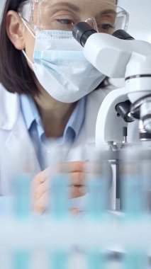 Laboratuvarda mikroskop kullanan kadın bilim adamı portresi. Laboratuvar gözlüklü bir kadına odaklan. Bilimsel bir ortamda örnekleri analiz ediyor..