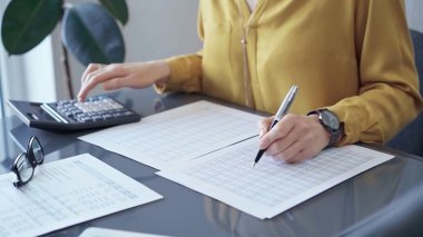 Sarı bluzlu profesyonel iş kadını mali raporlar üzerinde çalışıyor. Bir kadının hesap makinesini hesap denetimi ya da muhasebesi için kullanarak ellerini yakınlaştır.