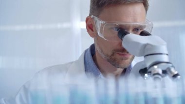 Koruyucu gözlüklü ve eldivenli bilim adamı laboratuvarda mikroskop kullanıyor. Araştırmacı portresi. Mikrobiyoloji bilim konsepti.