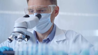 Koruyucu gözlüklü, maskeli ve eldivenli bilim adamı laboratuvarda mikroskop kullanıyor. Araştırmacı portresi. Mikrobiyoloji bilim konsepti.