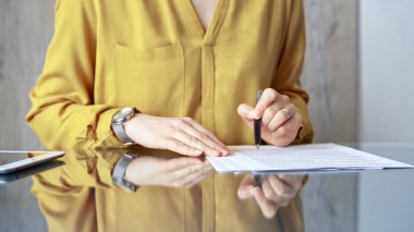 Sarı üniformalı bir iş kadını masadaki belgeleri analiz ediyor. Profesyonel bir denetçinin ya da avukatın ofis ortamında uzun bir evrak raporunu incelemesi. İş adamları konsepti.