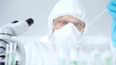 Prezervatif kullanan profesyonel bilim adamı pipetini kullanıyor ve laboratuvar ortamında test tüpünü inceliyor..