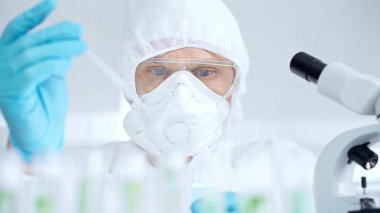 Prezervatif kullanan profesyonel bilim adamı pipetini kullanıyor ve laboratuvar ortamında test tüpünü inceliyor..