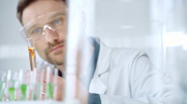 Güvenlik gözlüklü bir araştırmacı modern bir laboratuvarda turuncu bir sıvıyla laboratuvar tüpünü inceliyor. Bilim, mikrobiyoloji ve tıp.