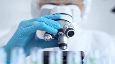 Koruyucu ekipman kullanan profesyonel bilim adamı bir laboratuvar ortamında mikroskop kullanıyor, yakın plan. Bilim ve tıp kavramları.