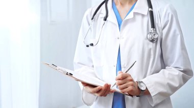 Doktor kadın panoya not alıyor. Tanımlanamayan profesyonel bir kadının yakın çekimi tıbbî form doldurur..
