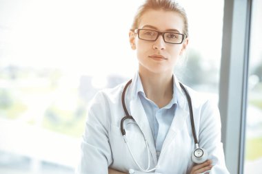 Steteskopla gülümseyen güzel kadın doktor güneşli hastanedeki hastalara yardım etmeye hazır. Tıp konsepti.