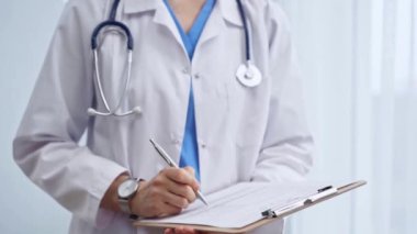 Kadın doktor not defterine not alıyor. Tanımlanamayan bir kadın sağlık hizmetleri uzmanının yakın plan fotoğrafı ve klinikte ayakta dururken ilaç geçmişi doldurma formu..