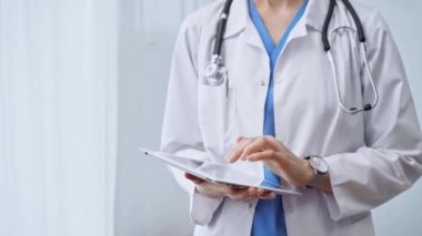 Klinikte dijital tablet kullanan kadın doktor. Boynuna steteskop takmış bir sağlık görevlisi cam arka planda dururken dokunmatik ekranlı bir bilgisayarı kullanıyor. İlaç ve...