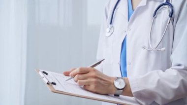 Kadın doktor not defterine not alıyor. Tanımlanamayan bir kadın sağlık hizmetleri uzmanının yakın plan fotoğrafı ve klinikte ayakta dururken ilaç geçmişi doldurma formu..