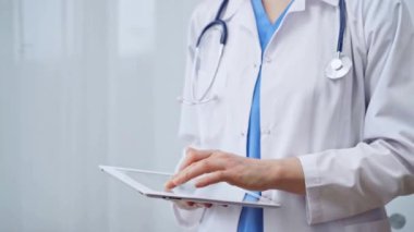 Klinikte dijital tablet kullanan kadın doktor. Boynuna steteskop takmış bir sağlık görevlisi cam arka planda dururken dokunmatik ekranlı bir bilgisayarı kullanıyor. İlaç ve...