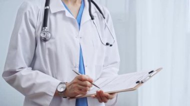 Kadın doktor not defterine not alıyor. Tanımlanamayan bir kadın sağlık hizmetleri uzmanının yakın plan fotoğrafı ve klinikte ayakta dururken ilaç geçmişi doldurma formu..