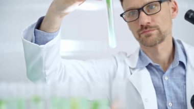 Laboratuvar tüpünü yeşil sıvıyla inceleyen bilim adamı. Mikrobiyoloji ve bilim konsepti.