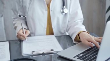 Doktor kadın laptopta tıbbi raporlarla çalışıyor. Sağlık bakımı uzmanı hasta dosyalarını inceler ve klinik ortamında veri girişi yapar. İlaç..