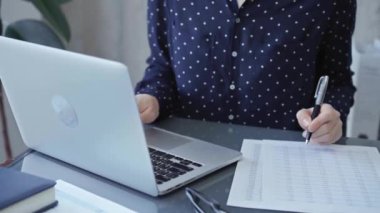 İş kadını profesyonel modern bir işyerindeki dizüstü bilgisayarın yanında mali evrakları kontrol ediyor. İş dünyasında denetim.