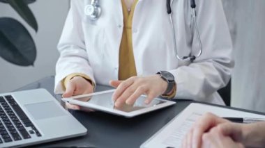 Tablet ve dizüstü bilgisayarı olan bir doktora danışıyorum. Dijital cihazlar kullanarak tedavi seçeneklerini tartışan bir sağlık uzmanı. İlaç ve sağlık hizmetleri kavramı.