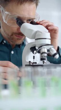 Koruyucu gözlüklü bilim adamı laboratuvarda mikroskop kullanıyor. Mikrobiyoloji bilim konsepti.