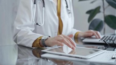 Doktor kadın muayenehanedeki cam masada tablet kullanıyor. Klinikte bir doktorun elleri dokunmatik ped ile etkileşime giriyor. İlaç ve sağlık hizmetleri.