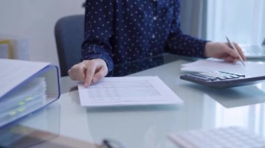 Kadın bir muhasebeci ofisteki cam bir masadaki vergileri hesaplamak için dizüstü bilgisayar ve hesap makinesi kullanıyor. İş denetimi ve finansman yapan bir kadın.
