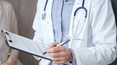 Doktor ve hasta. Arka planda bir kadın olan bir doktorun el resmi panoya not alıyor. İlaç ve Sağlık Hizmetleri.