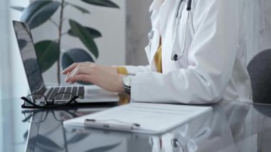 Dokümanların yanında duran dizüstü bilgisayar ve steteskop kullanan bir doktorla profesyonel sağlık hizmeti ayarları. İlaç ve Sağlık Hizmetleri