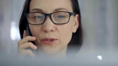 Gözlüklü, gülümseyen bir kadın cep telefonu kullanıyor, geçmişi bulanık. Yaşam tarzı ve iş kavramları.