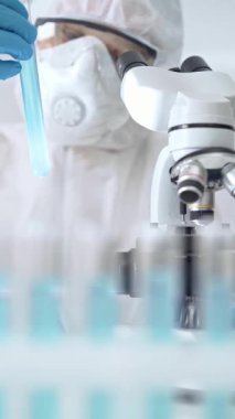 Profesyonel bilim adamı, mikroskobun yanındaki tüp örneğini dikkatlice analiz ediyor.