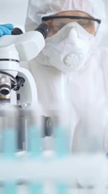 Profesyonel bilim adamı, mikroskobun yanındaki tüp örneğini dikkatlice analiz ediyor.