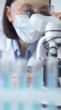 Laboratuvar gözlüklü bir kadına odaklan. Bilimsel bir ortamda mikroskop kullanarak örnekleri analiz et.