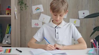Arka planda bitkiler ve oyuncaklar olan düzenli bir masadaki deftere yazan odaklanmış çocuk.